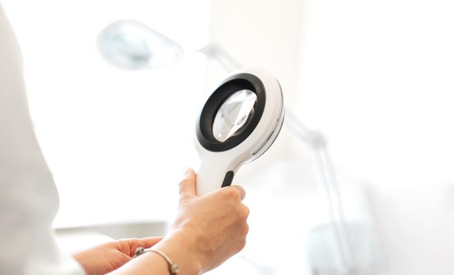 Doctor trichologist dermatologist holding a magnifying glass for examination of a patient.